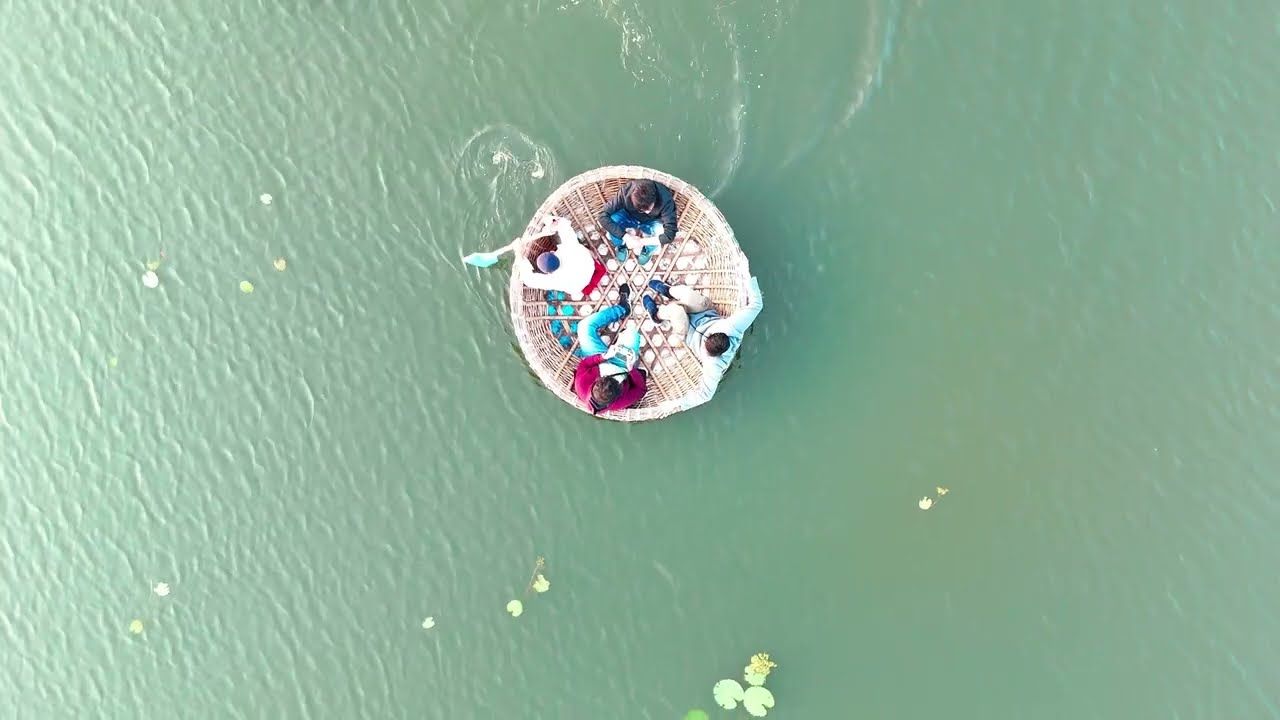 Aerial shot of a round coracle boat on the green water of the Tungabhadra river